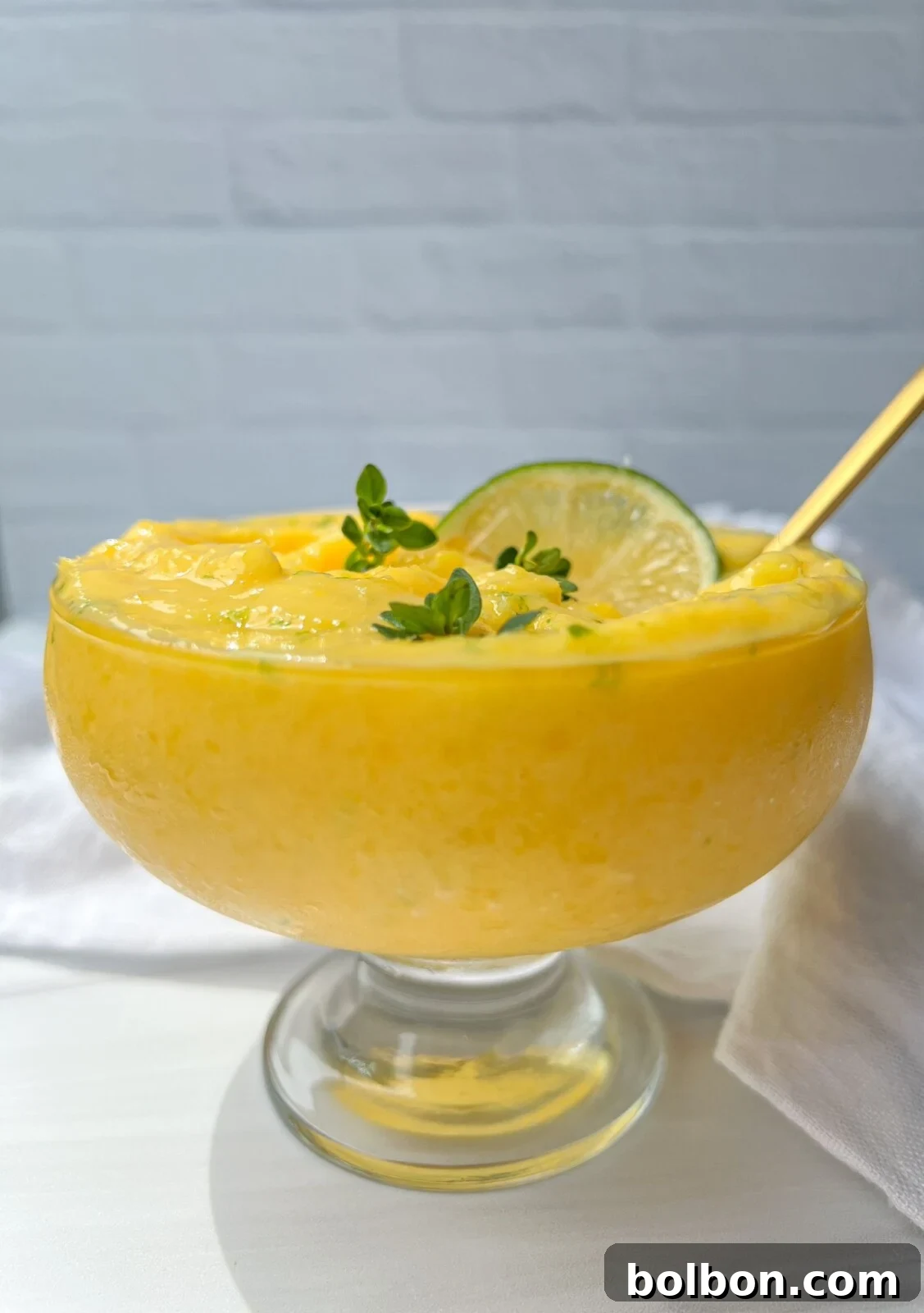 Creamy homemade mango frozen yogurt in a bowl, garnished with fresh lime and mint, ready to be enjoyed.