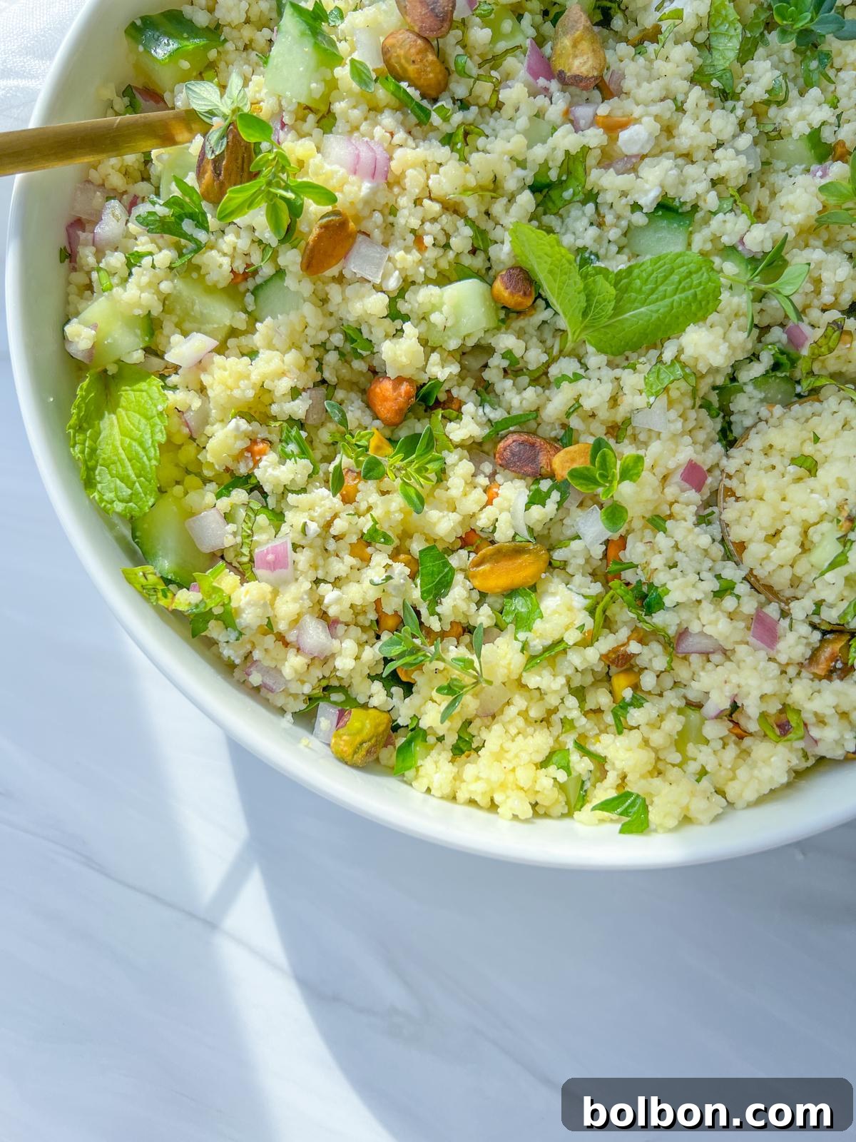 Jennifer Aniston Couscous Salad, a vibrant mix of fluffy couscous, fresh vegetables, aromatic herbs, crumbled feta, and crunchy pistachios, served in a white bowl.