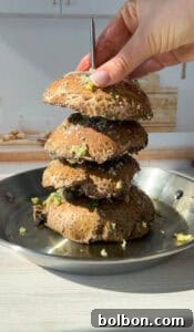 A stack of four seasoned portobello mushrooms is held vertically by a hand with a metal skewer. The mushrooms are in a round metal pan, sprinkled with herbs and garlic, and lit by natural sunlight.