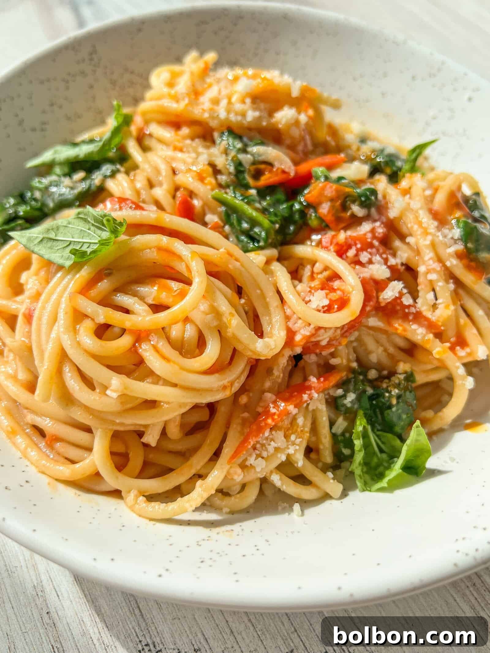 Rich and Creamy Meghan Markle Pasta Ready to Serve with Fresh Basil A plate of spaghetti topped with tomato sauce, fresh basil leaves, and grated cheese. The noodles are neatly arranged, garnished with vibrant green herbs, and the dish is presented in a white speckled bowl on a light-colored surface. The Meghan Markle Pasta Recipe is a must try!