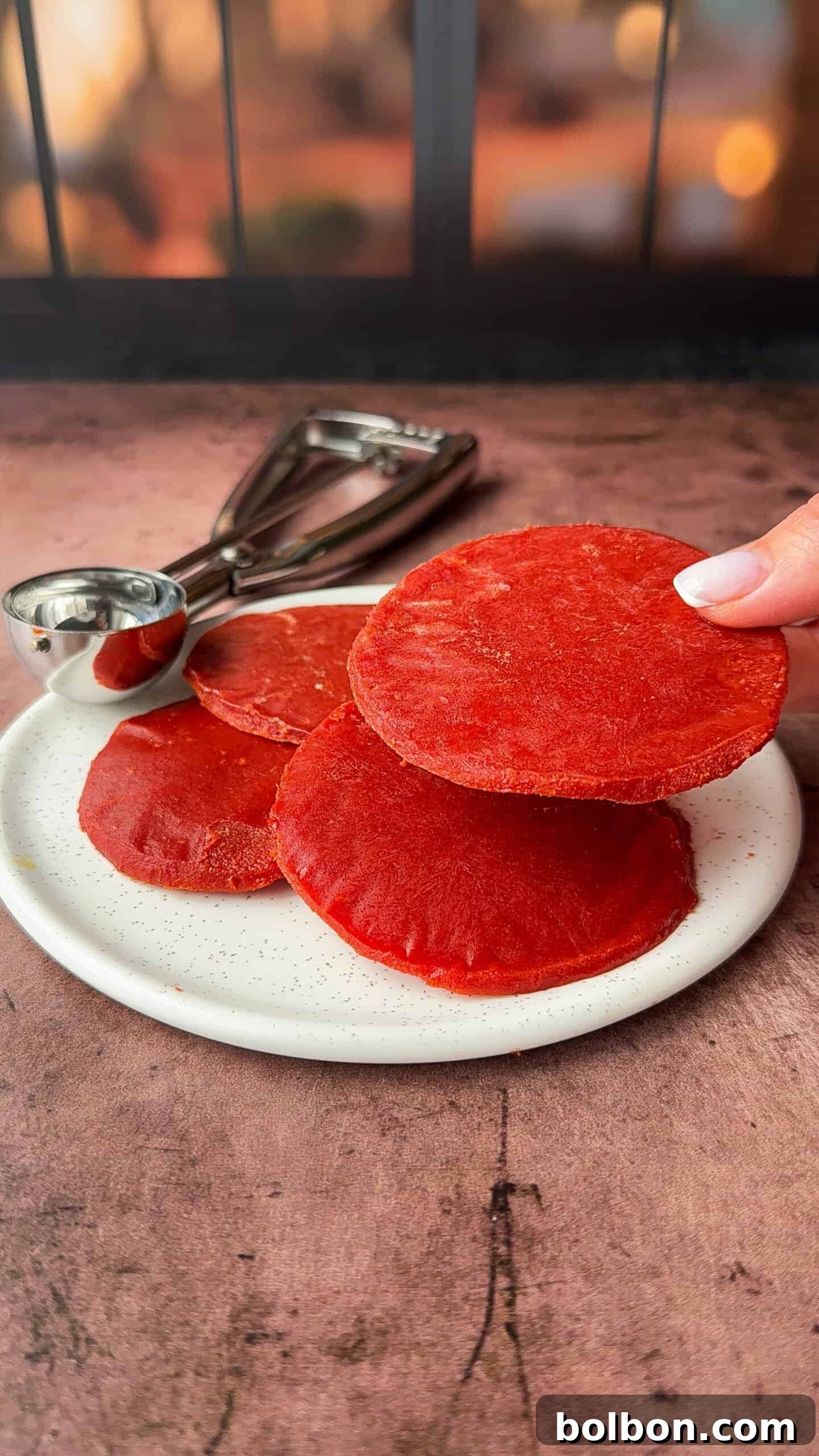 Genius Tomato Paste Tips 7 Close-up of a hand holding the red tomato paste circle above a white plate.