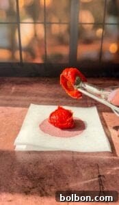 Genius Tomato Paste Tips 3 A small metal scoop holds a portion of red tomato paste in a sunlit setting. Below it, there's a dollop of tomato paste placed on a white square of parchment paper against a warm, softly lit background.