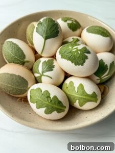 Doğanın Renkleriyle Paskalya Yumurtaları 8 A bowl containing white eggs decorated with green leaf patterns, placed on a textured ceramic dish. The background is light and minimalistic, enhancing the natural appearance of the eggs.