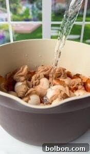 Doğanın Renkleriyle Paskalya Yumurtaları 9 Water being poured into a bowl containing several wrapped bundles of eggs. The eggs appear to have a natural dye covering, and the preparation is part of a decorative or dyeing process. The scene is set in a bright, airy environment.