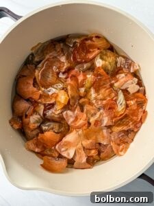 Doğanın Renkleriyle Paskalya Yumurtaları 10 A beige pot filled with soaking onion skins in water, featuring shades of brown and orange. The scene is lit with natural light.