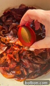 Doğanın Renkleriyle Paskalya Yumurtaları 11 Hand holding a small strainer above a pot filled with reddish-brown onion skins submerged in water, bathed in warm, natural light.