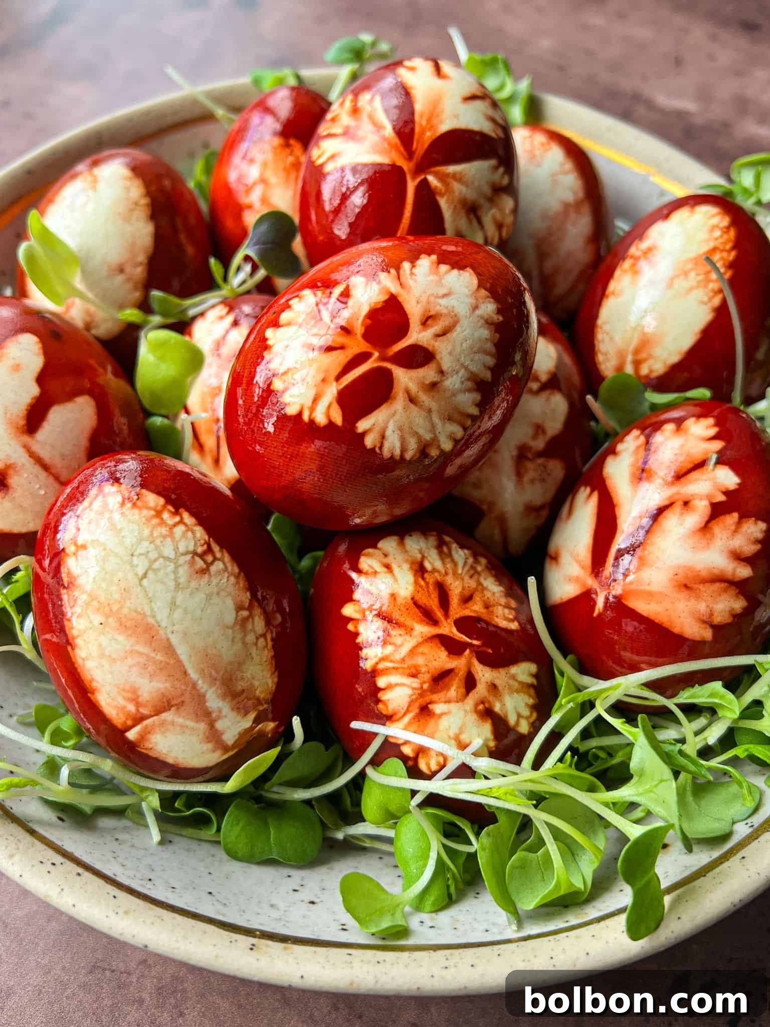 Doğanın Renkleriyle Paskalya Yumurtaları 3 A bowl of red-brown eggs featuring intricate leaf patterns, nestled on a bed of fresh green sprouts. The eggs have a marbled appearance, showcasing a variety of natural textures.