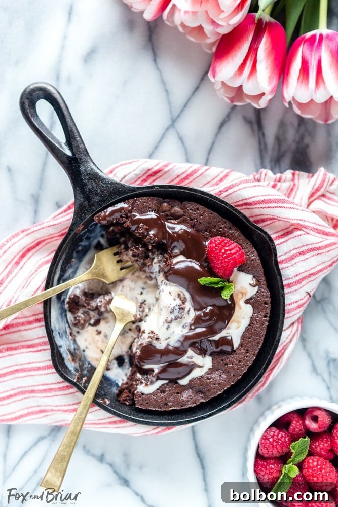 Warm raspberry swirl brownie sundae in a skillet topped with vanilla ice cream and hot fudge, perfect for a romantic dessert.