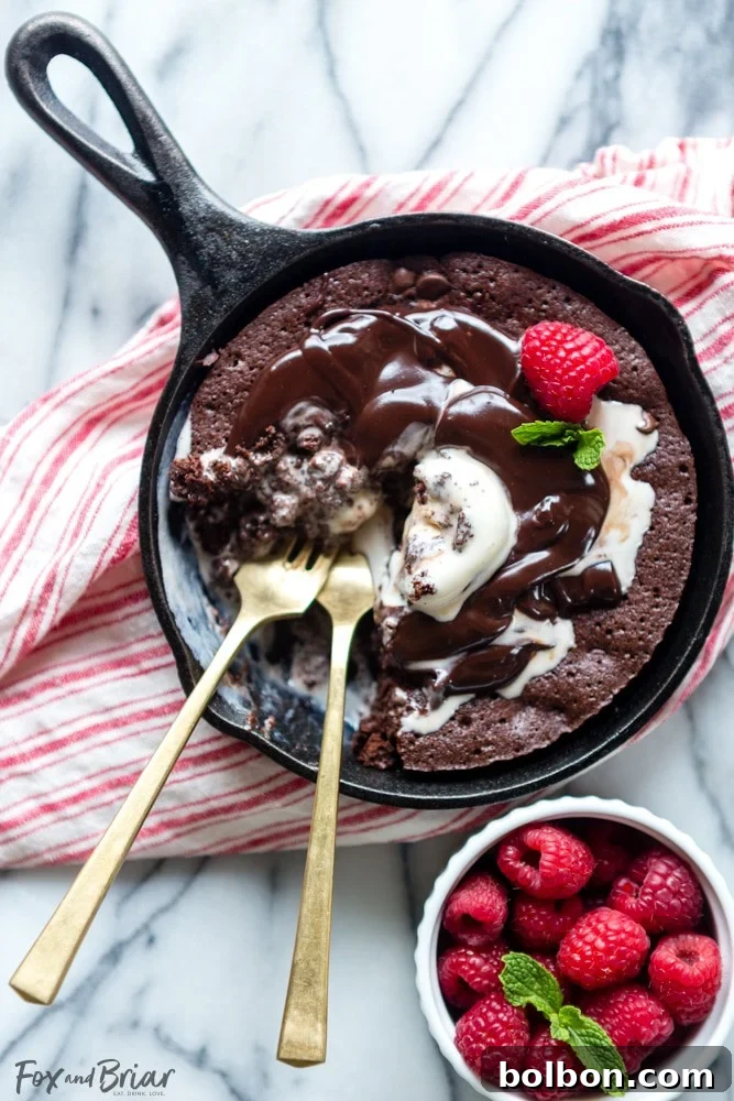 Overhead view of a prepared raspberry swirl brownie sundae with two scoops of vanilla ice cream and hot fudge drizzle.