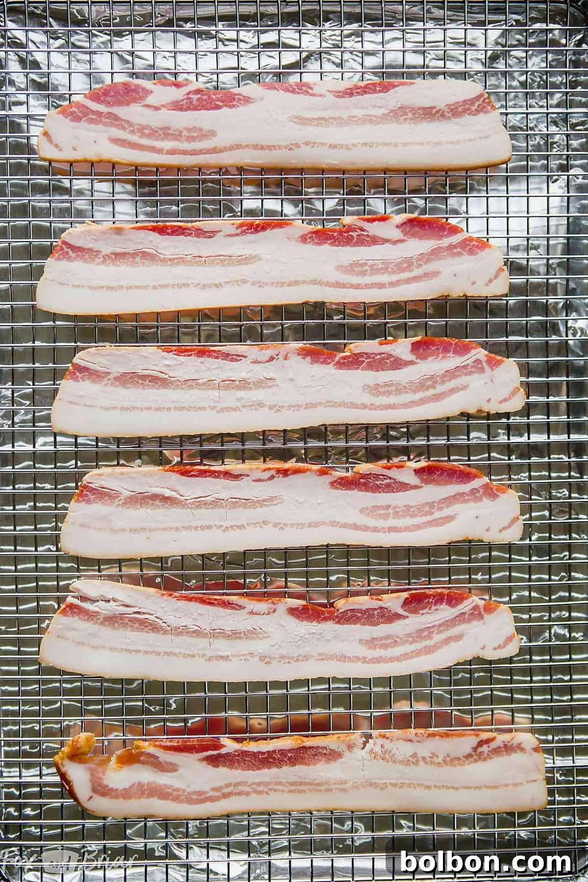 Raw thick-cut bacon slices arranged on a wire rack, ready for the oven.