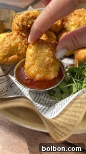 A hand dips a golden, crispy nugget into a small cup of reddish sauce, with more nuggets and some fresh greens on a tray lined with printed parchment paper.