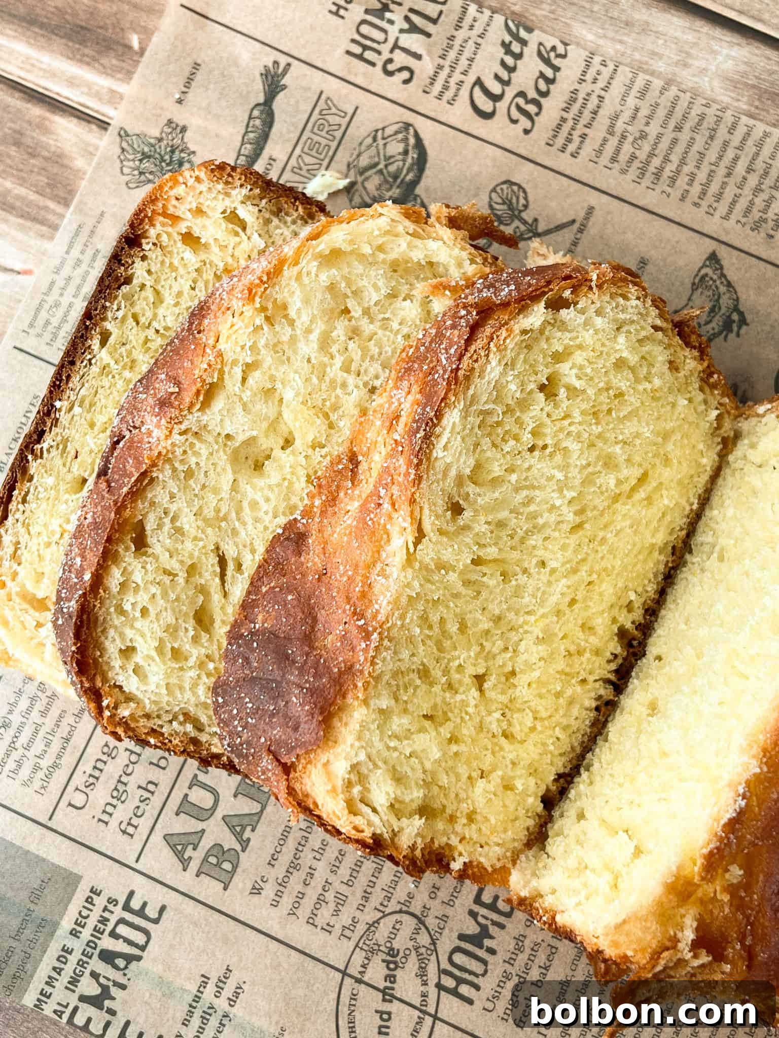 Three thick slices of golden, crusty No Knead Easter bread with a fluffy, airy texture are arranged on vintage-style printed parchment paper over a wooden surface.