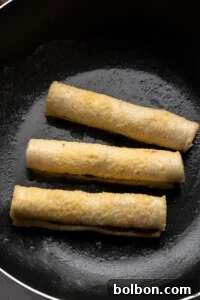 Three French Toast Rollups are being fried in a black skillet, lightly browned and sizzling in oil.