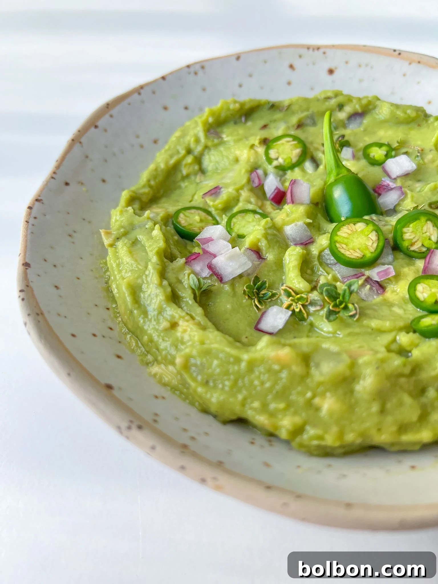 Freshly made green guacamole in a white bowl, garnished with a lime wedge and cilantro sprigs, served with a pile of tortilla chips on the side.