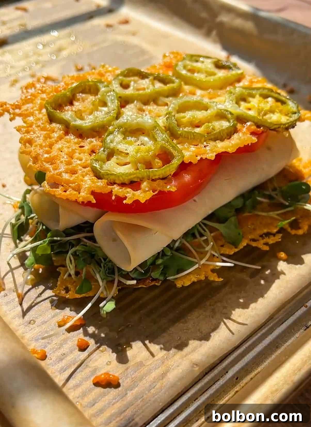 Jalapeño Hype Sandwich 3 A sandwich with microgreens, rolled turkey slices, tomato, and crispy baked cheese topped with jalapeño slices, served on parchment paper.