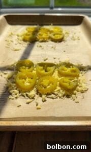 Jalapeño Hype Sandwich 4 Sliced pickled jalapeños arranged on small piles of shredded cheese on a parchment-lined baking sheet, with sunlight streaming across the tray.