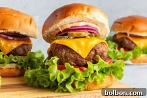 Three mouth-watering cheeseburgers, generously layered with fresh lettuce, ripe tomato slices, melted cheese, tangy pickles, and crisp red onion, all crowned with a creamy sauce and served in perfectly toasted buns, artfully displayed on a rustic wooden board.