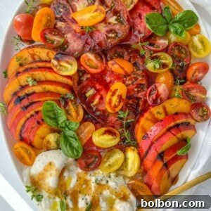 A vibrant Burrata Tomato Peach Salad with heirloom tomatoes, peaches, cherry tomatoes, fresh basil, and burrata cheese, drizzled with olive oil, served on a white plate with a gold fork.