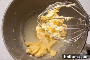 Churning Your Own Golden Butter 6 A close-up of a metal mixing bowl and whisk attachment with yellow butter and white liquid, likely separated during mixing.