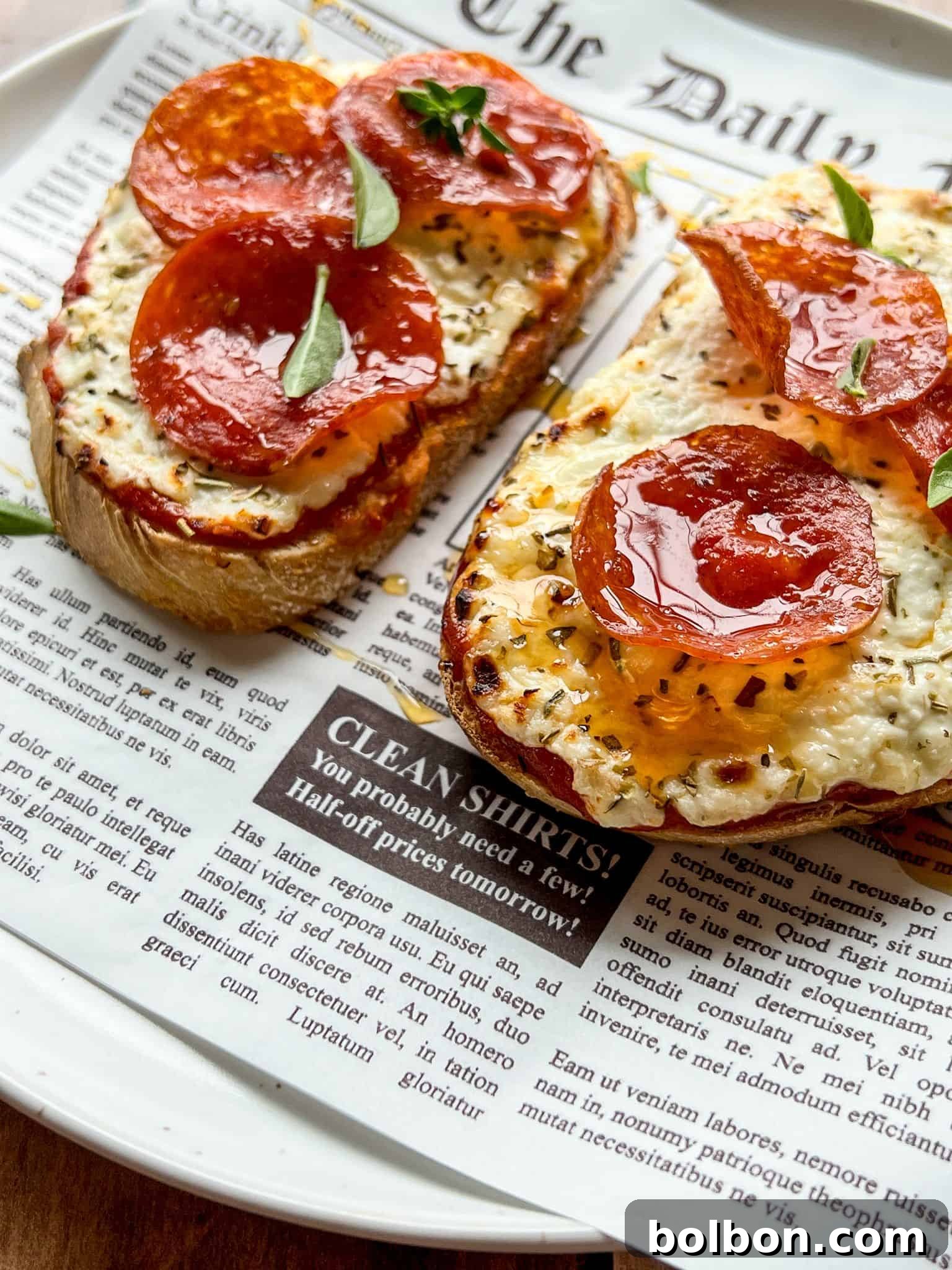 Creamy Cottage Cheese Toast Pizzas 3 Two slices of toasted bread with melted cheese and pepperoni, garnished with fresh herbs, served on a plate lined with newspaper-style parchment.