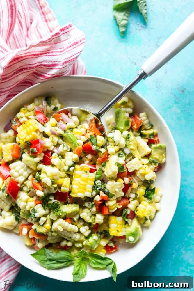 Vibrant and fresh summer corn salad with avocado, red bell pepper, and basil in a white bowl, perfect for a BBQ or picnic.