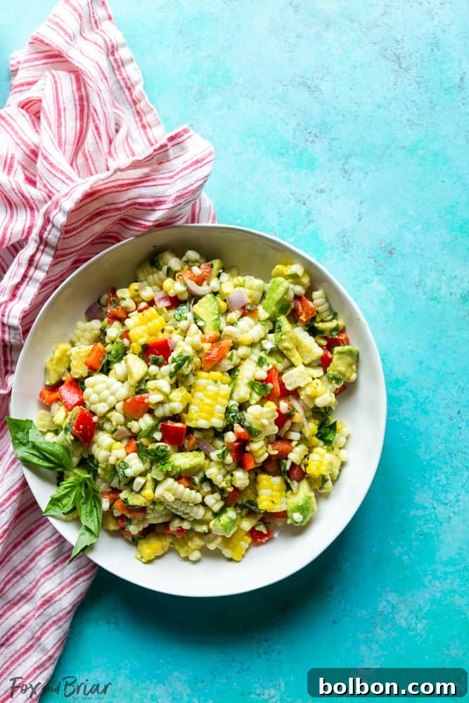 Close-up of fresh summer corn salad with vibrant kernels, diced avocado, red bell pepper, and green basil leaves.