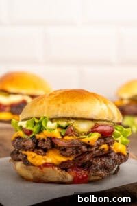 A close-up of a cheeseburger with two beef patties, melted cheddar cheese, lettuce, pickles, onions, ketchup, and mayonnaise in a shiny brioche bun. Two more burgers are blurred in the background.