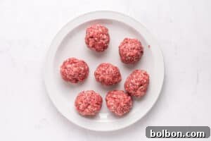 A white plate with seven raw ground beef meatballs arranged in a circular pattern on a light marble surface.