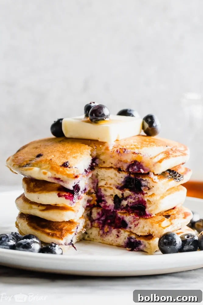 Berry Burst Buttermilk Pancakes 8 A plate with a stack of buttermilk blueberry pancakes and a side of crispy bacon