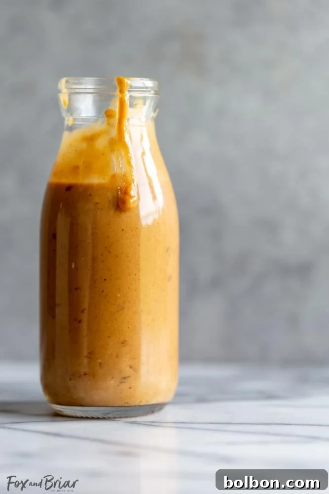 All the fresh and pantry ingredients for a homemade Thai Peanut Sauce laid out on a kitchen counter, including jars of peanut butter, soy sauce, rice vinegar, fresh lime, ginger, and garlic.