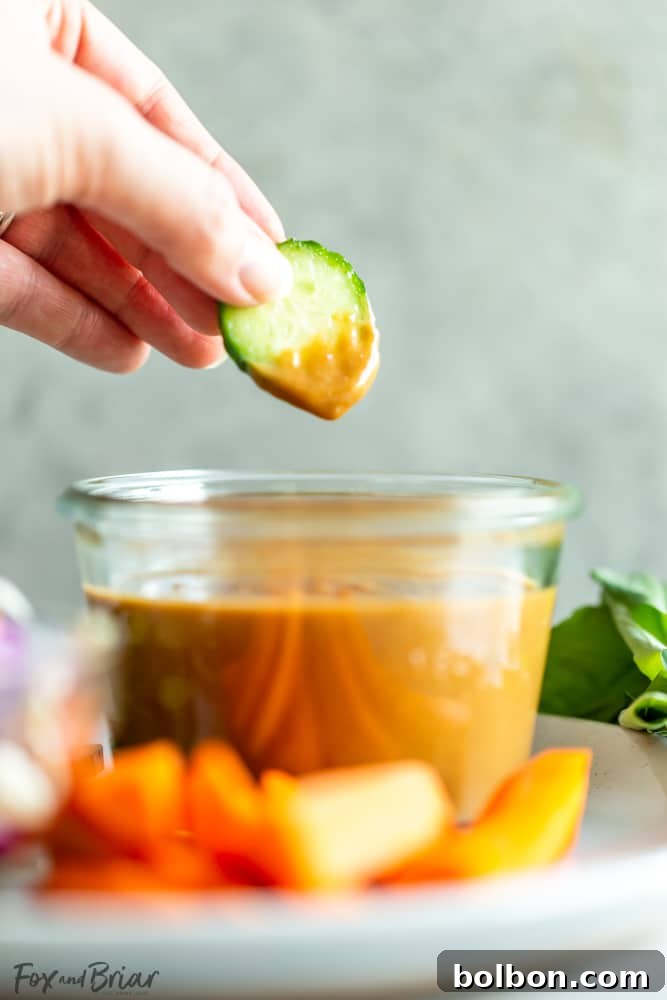 A vibrant bowl of homemade Thai Peanut Sauce, expertly prepared and garnished with chopped peanuts, fresh cilantro, and a lime slice, showcasing its appetizing appeal.