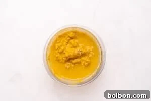 A glass bowl filled with chunky, golden-yellow liquid, possibly a curry or sauce, placed on a white marble surface.