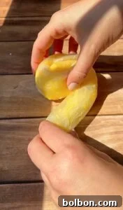 Crispy Rice Paper Burek 8 A person shapes a piece of yellow dough on a wooden surface, using both hands. Sunlight casts shadows on the table and hands.