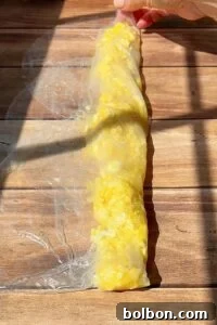 Crispy Rice Paper Burek 6 A hand rolls a translucent rice paper sheet filled with scrambled eggs on a wooden surface, in bright sunlight with visible shadows.