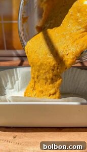 Decadent Pumpkin Bread with Cream Cheese 12 Bright yellow-orange batter is being poured from a bowl into a rectangular paper-lined baking dish, with sunlight casting shadows across the scene.