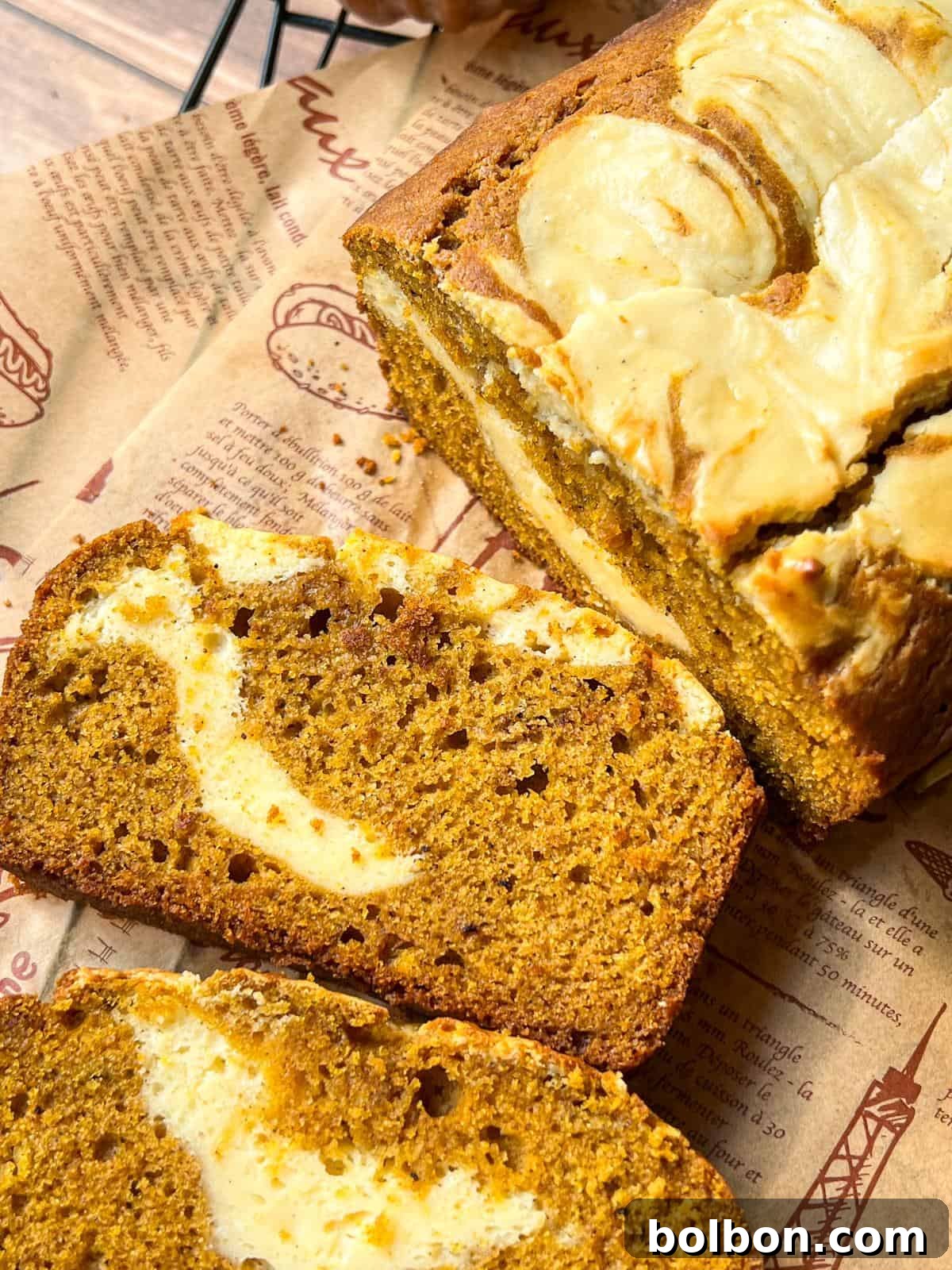 Decadent Pumpkin Bread with Cream Cheese 4 A close-up of sliced pumpkin bread with swirls of cream cheese, placed on brown printed parchment paper. The bread has a moist texture and rich, golden-brown color.