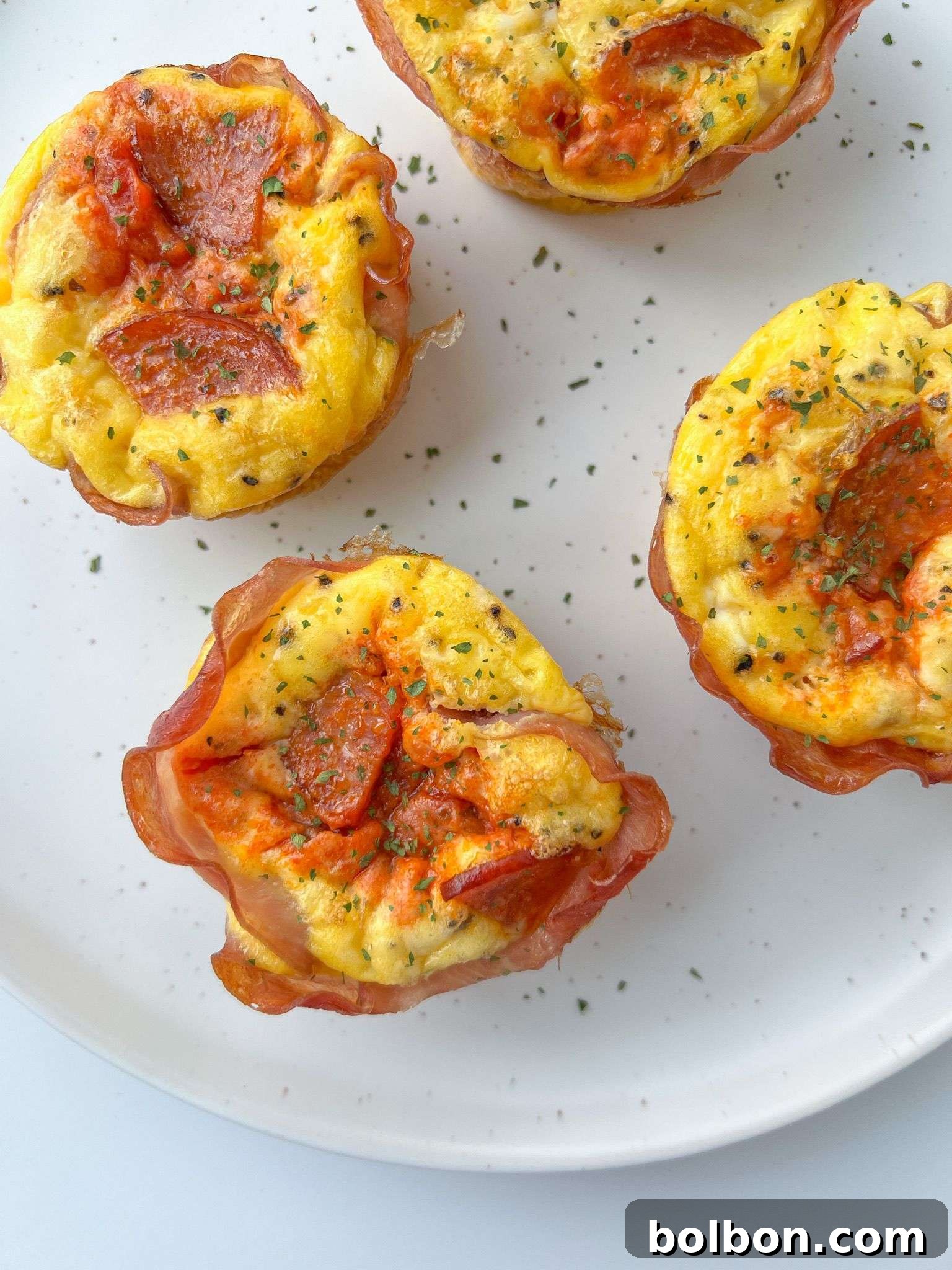 Pizza egg muffins on a white plate, garnished with fresh herbs, showcasing their golden-brown tops and rich centers.