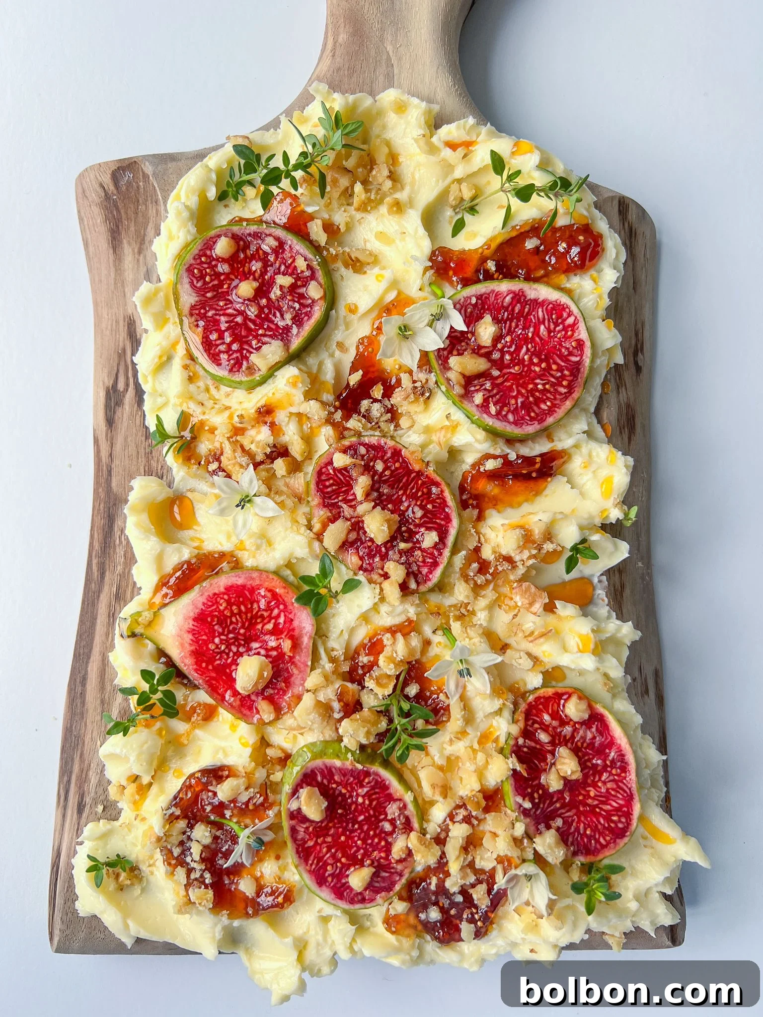 A beautifully arranged butter board with swirls of softened butter, fresh figs, crunchy walnuts, flaky sea salt, and a drizzle of hot honey, served on a rustic wooden board.