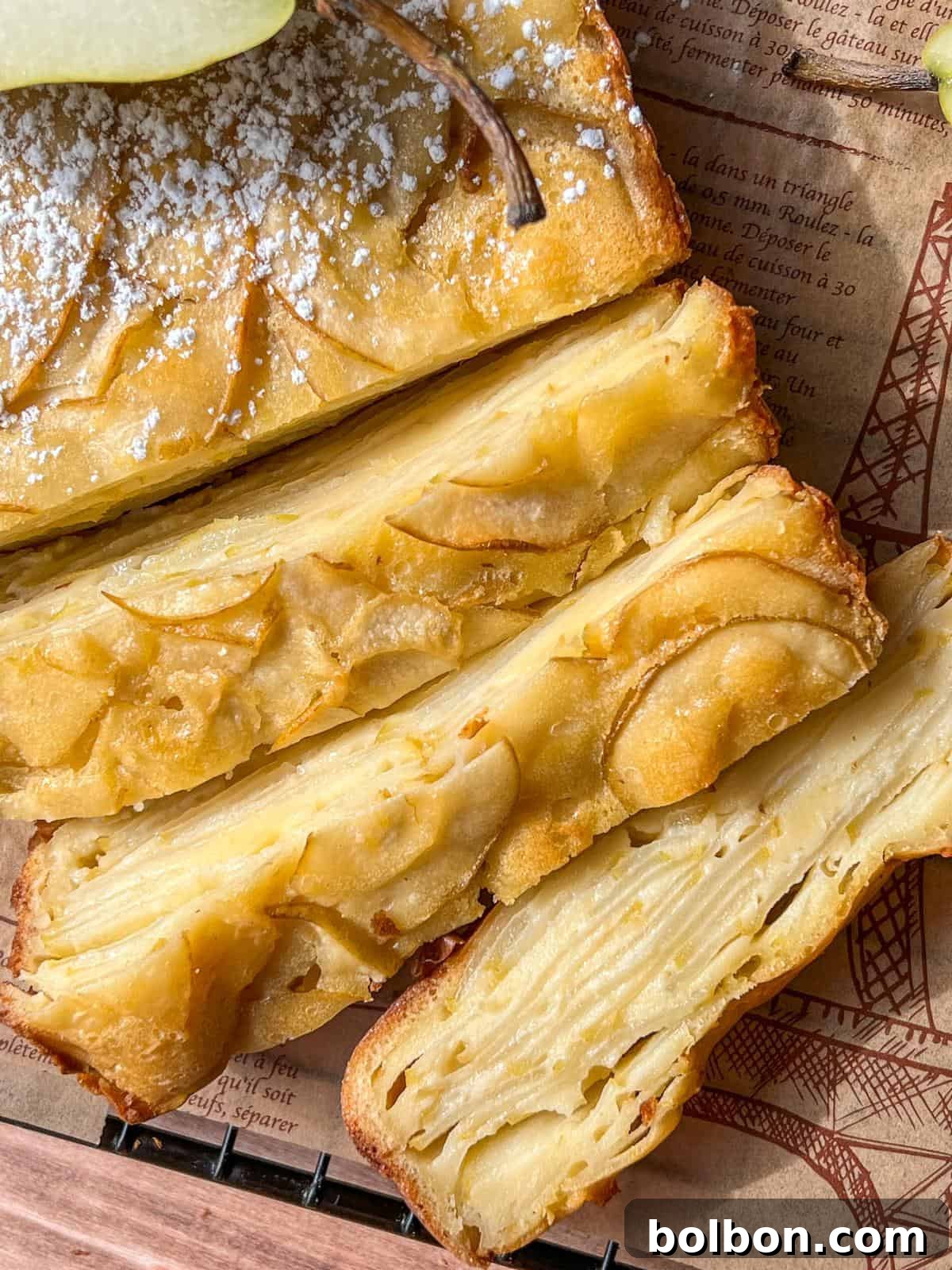 A close-up shot of multiple slices of a golden-baked Invisible Pear Cake, beautifully layered with thin apple slices throughout its rich interior. Each slice is elegantly dusted with powdered sugar and arranged on a sheet of decorative parchment paper, highlighting its intricate texture and inviting appeal.