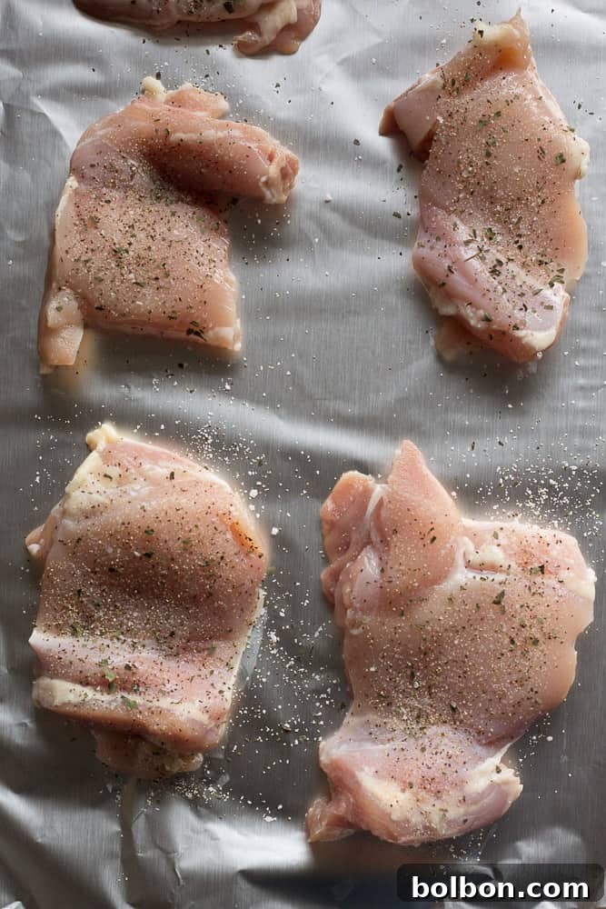 Raw chicken thighs on aluminum foil, seasoned with Greek spices. Ready for skillet cooking.