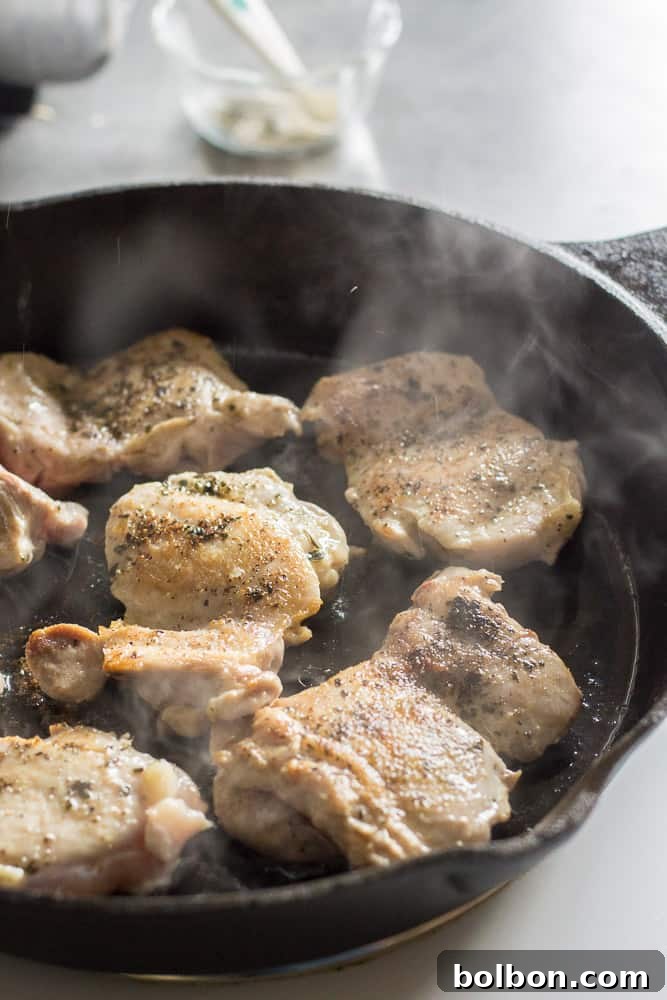 Frying Greek chicken thighs in a cast iron skillet, showing the golden-brown sear. One pan dinner, quick and easy meal.