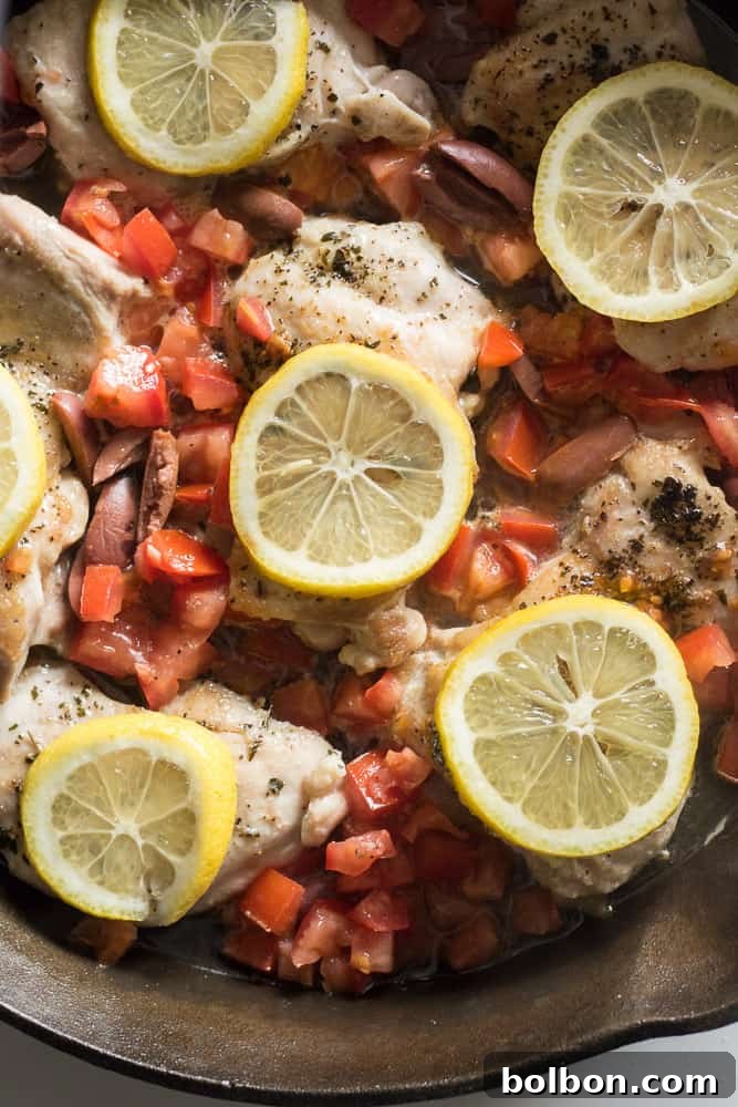 Finished Greek Chicken Thighs dish in a cast iron skillet, with lemon slices, Kalamata olives, and tomatoes, garnished with parsley. A complete one-pan weeknight meal.