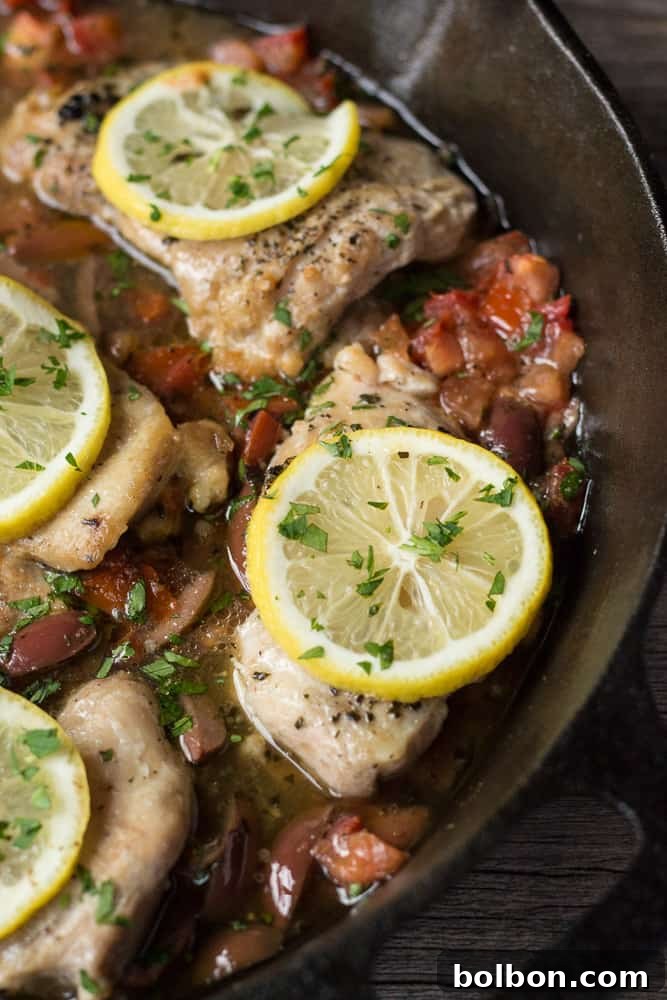 A close-up shot of cooked Greek Chicken Thighs, garnished with fresh parsley, ready to be served from a cast iron skillet. Healthy and delicious weeknight dinner.