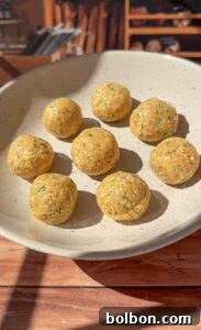 A beige plate holds eight round, yellowish snack balls with green flecks, arranged neatly—reminiscent of Authentic Matzo Ball Soup. The plate sits on a wooden surface, set against a softly blurred, rustic background.