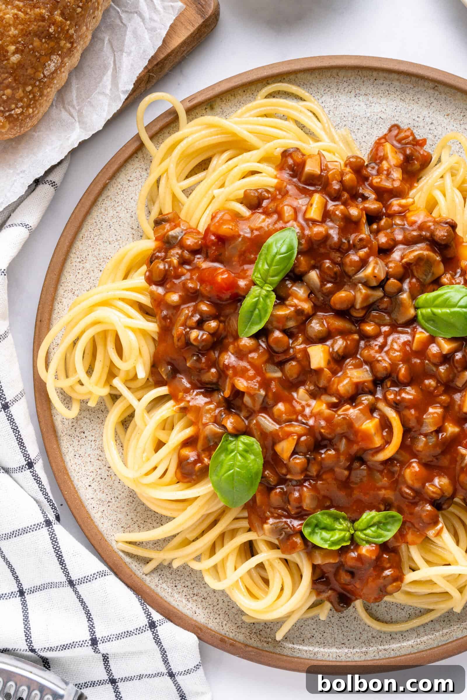 A plate with spaghetti, lentil bolognese and basil on top, ready to be enjoyed.