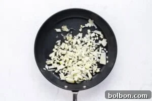 Chopped onions being sautéed in a black frying pan on a white surface.