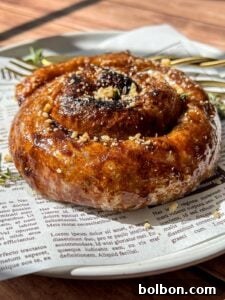 Golden Rice Paper Apple Delights 11 A close-up of a glazed cinnamon roll topped with crushed nuts, served on a white plate lined with newspaper print, with a fork and sprigs of thyme in the background.