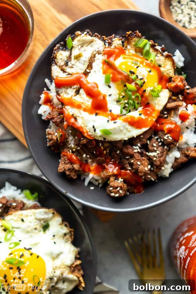 Quick Korean Beef Bowls 3 Close-up of a Korean Ground Beef Bowl featuring a runny fried egg drizzled with sriracha, showcasing the rich texture of the ground beef and rice underneath.
