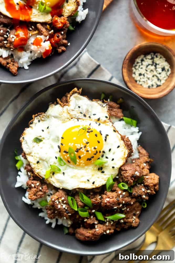 Quick Korean Beef Bowls 4 Overhead shot of a Korean Ground Beef Bowl, highlighting the golden fried egg, sprinkled with black sesame seeds and finely chopped green onions, on a bed of flavorful beef and rice.
