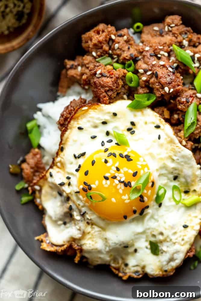 Quick Korean Beef Bowls 6 A close-up view of a perfectly fried egg, its golden yolk slightly runny, resting atop a bed of savory Korean Ground Beef and fluffy white rice, garnished with black sesame seeds, ready to be enjoyed.